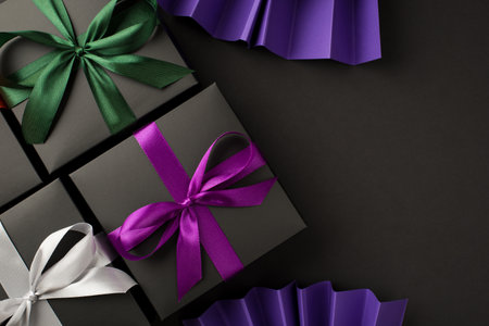 Top view photo of three black gift boxes with violet green and white ribbon bows and violet paper...