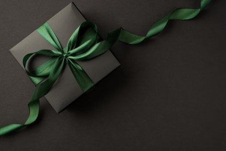Top view photo of stylish black giftbox with green satin ribbon bow on isolated black background with empty spaceの写真素材