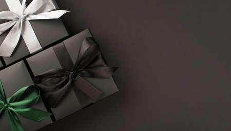 Top view photo of three stylish black gift boxes with black white and green ribbon bows on isolated black background with copyspaceの写真素材