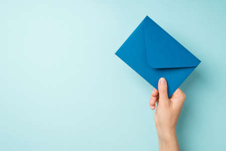 First person top view photo of hand holding closed blue envelope on isolated pastel blue background with copyspaceの写真素材