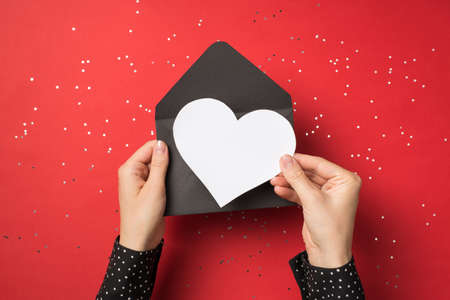 First person view above photo of female hands holding black envelope with white card as heart inside...
