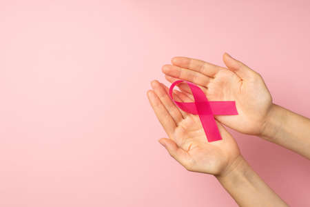 First person top view photo of hands holding pink satin ribbon in palms symbol of breast cancer awareness on isolated pastel pink background with copyspaceの写真素材