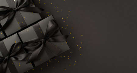 Top view photo of black gift boxes with black ribbon bow tag and golden confetti on isolated black...