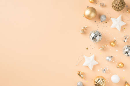 Top view photo of white golden and silver christmas tree decorations stars disco balls sequins and serpentine on isolated beige background with blank spaceの写真素材