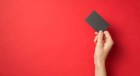 First person top view photo of hand holding black plastic card on isolated red background with empty spaceの写真素材