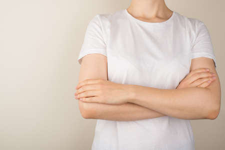 Cropped closeup photo of young woman in white t-shirt with crossed arms on isolated gray background with empty spaceの写真素材