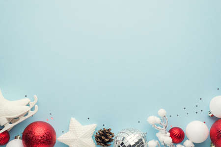 Top view photo of white and red christmas tree decorations disco ball star snowy branch small ice skates and sequins on isolated pastel blue background with empty spaceの写真素材