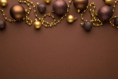 Top view photo of golden and brown christmas tree balls and gold beard garland on isolated brown background with copyspaceの写真素材