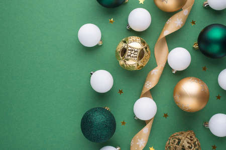 Top view photo of gold white and green christmas tree decorations balls ribbon serpentine and stars confetti on isolated green background with blank spaceの写真素材