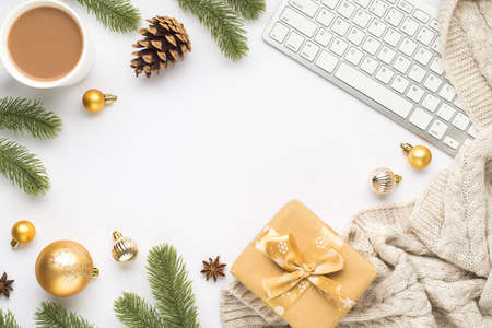 Top view photo of keyboard, cup of hot drinking, gold christmas tree balls, pine twigs cone, anise sweater and giftbox on isolated white background with copyspace in the middleの写真素材