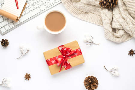 Top view photo of notepad pen keyboard cup of hot drinking snow twigs pine cones anise cozy sweater and giftbox with red bow on isolated white backgroundの写真素材
