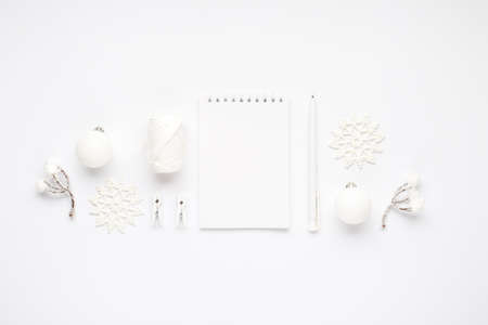 Top view photo of white christmas tree decorations, notepad, pen, snowflakes balls, snow twigs spool of thread and clothespins on isolated white background with copyspaceの写真素材