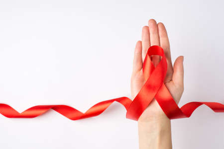 First person top view photo of female hand holding curly red ribbon in palm symbol of aids awareness on isolated white background with empty spaceの写真素材