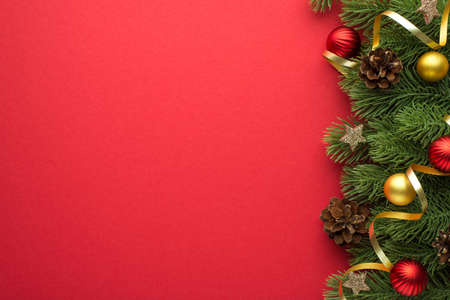 Top view photo of gold and red christmas tree balls pine cones glowing stars and gold serpentine on pine branches on isolated red background with empty spaceの写真素材