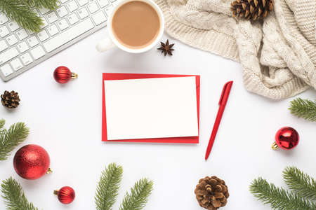 Top view photo of red envelope paper sheet pen keyboard cup of hot drinking red christmas tree balls pine twigs cones anise and cozy sweater on isolated white background with copyspaceの写真素材