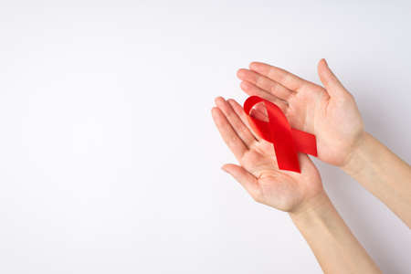 First person top view photo of female hands demonstrating red ribbon in palms symbol of aids...