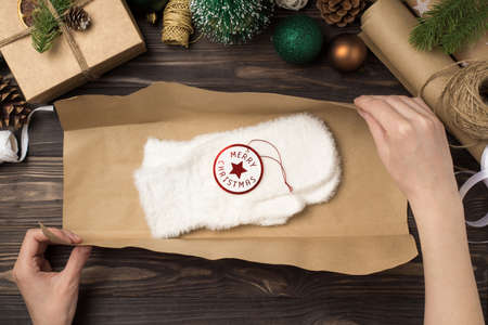 First person top view photo of woman's hands packing white fluffy mittens with tag merry christmas...