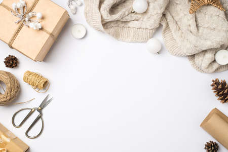 Top view photo of craft paper giftbox with snow twig sweater christmas tree balls handicraft tools scissors spools of twine candles and cones on isolated white background with copyspaceの写真素材