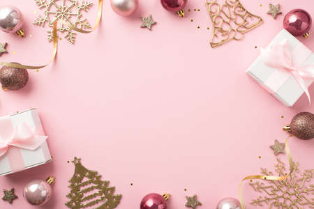 Top view photo of christmas decorations pink balls gold bell pine snowflake shaped ornaments white gift boxes stars serpentine sequins on isolated pastel pink background with copyspace in the middle mock upの写真素材