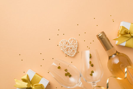 Top view photo of valentine's day decor white gift boxes with golden bows wine bottle rattan heart wineglasses with heart shaped confetti and sequins on isolated pastel beige background with copyspaceの写真素材