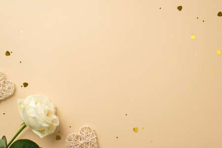 Top view photo of white rose golden sequins heart shaped confetti and rattan hearts on isolated beige background with empty spaceの写真素材