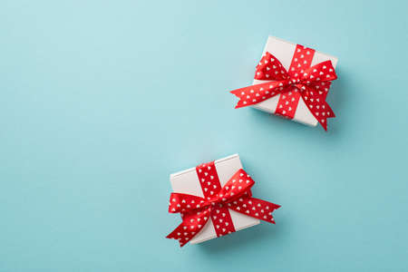 Top view photo of valentine's day decorations two white gift boxes with red ribbon bows heart pattern on isolated pastel blue background with blank spaceの写真素材
