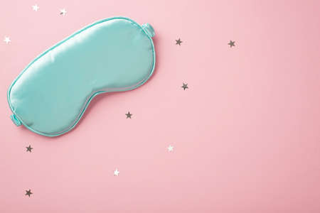 Top view photo of blue silk sleeping mask and star shaped confetti on isolated pastel pink background with copyspaceの写真素材