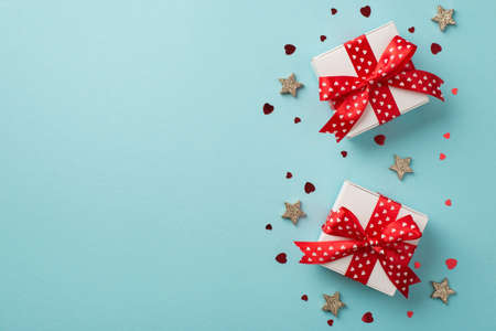 Top view photo of st valentine's day decorations two white gift boxes with red ribbon bows glowing stars and heart shaped confetti on isolated pastel blue background with empty spaceの写真素材