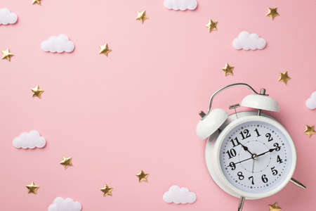 Top view photo of white alarm clock golden stars and clouds on isolated pastel pink background with blank spaceの写真素材