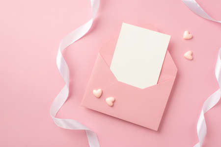 Top view photo of open pink envelope with paper sheet small pink hearts and white ribbon on isolated pastel pink background with copyspaceの写真素材