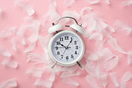 Top view photo of white alarm clock and pink feathers on isolated pastel pink backgroundの写真素材
