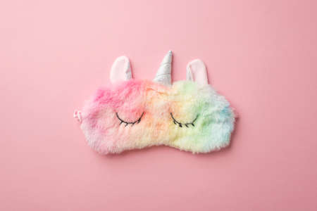 Top view photo of funny multicolored fluffy unicorn sleeping mask on isolated pastel pink backgroundの写真素材