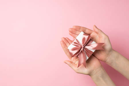 First person top view photo of saint valentine's day decorations young woman's hands giving small white giftbox with pink ribbon bow on isolated pastel pink background with copyspaceの写真素材