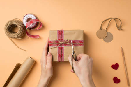 First person top view photo of valentine's day decor female hands cutting twine on craft paper...