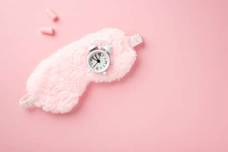Top view photo of pink fluffy sleeping mask small white alarm clock and earplugs on isolated pastel pink background with copyspaceの写真素材