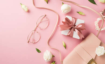 Top view photo of woman's day composition pink leather handbag stylish glasses white giftbox with bow scrunchies and white prairie gentian flower buds on isolated pastel pink background with copyspaceの写真素材