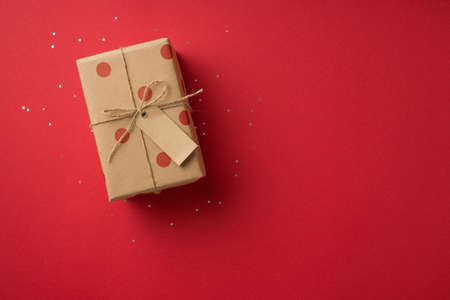 Top view photo of valentine's day decorations shiny sequins and craft paper giftbox with polka dot pattern and twine bow on isolated red background with copyspaceの写真素材