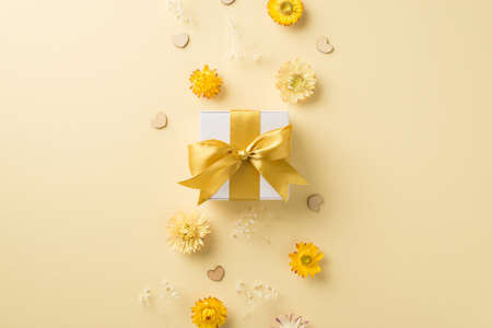 Top view photo of woman's day composition white giftbox with yellow bow hearts and wild flowers on isolated beige background with copyspaceの写真素材