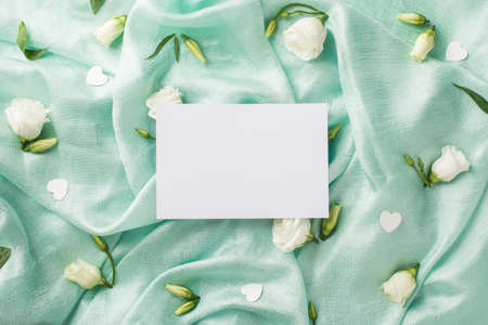 Top view photo of the one card and beautiful white eustomas with flower buds and confetti in shape of hearts scattered on the folds of the textured pastel turquoise background copyspaceの写真素材