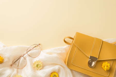 Top view photo of woman's day composition yellow leather handbag stylish glasses and field flowers on white scarf on isolated beige background with empty spaceの写真素材