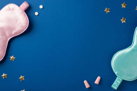 Top view photo of shapes of two silk silk masks pink and light blue one and two pink earplugs with two drugs and a confetti in shape of golden stars on the deep blue isolated background copyspaceの写真素材