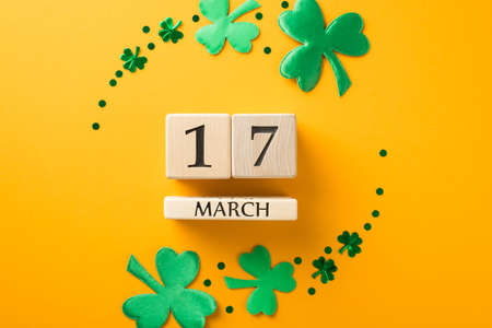 Top view photo of saint patricks day circle composition wooden cubes calendar with date 17 march surrounded by green shamrocks and confetti on isolated yellow backgroundの写真素材