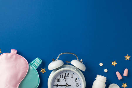 Top view photo of shapes of two silk masks pink and light blue one big white alarm and two pink earplugs with tube and two drugs and a confetti in shape of golden stars on the deep blue isolated background blank spaceの写真素材