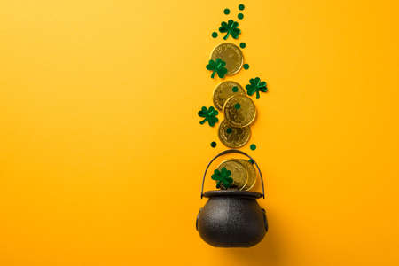 Top view photo of st patrick's day decorations shamrocks confetti and gold coins flying out of pot on isolated yellow background with copyspaceの写真素材