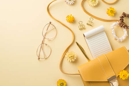 Top view photo of woman's day composition yellow leather purse stylish glasses scrunchies notebook golden pen binder clips and field flowers on isolated beige background with copyspaceの写真素材
