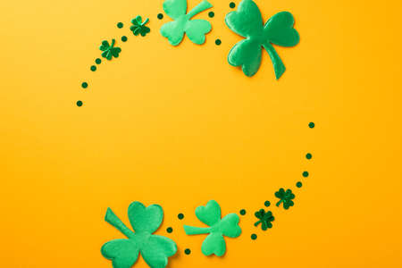 Top view photo of st patricks day circle composition green shamrocks and confetti on isolated yellow background with empty spaceの写真素材