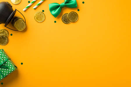 Top view photo of st patrick's day decorations giftbox straws green bow-tie confetti and pot with gold coins on isolated yellow background with copyspaceの写真素材