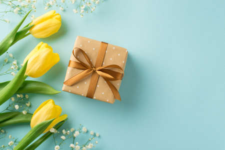 Top view photo of woman's day composition beige giftbox with brown ribbon bow yellow tulips and white gypsophila on isolated pastel blue background with blank spaceの写真素材