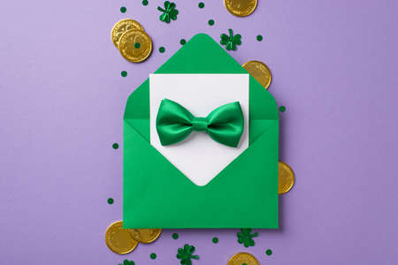 Top view photo of the green envelope with white card inside and tie bow on it with golden coins and...