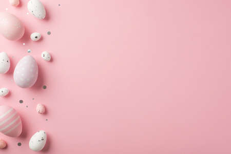 Top view vertical photo of easter decorations shiny confetti lilac pink and white easter eggs on isolated pastel pink background with copyspaceの写真素材